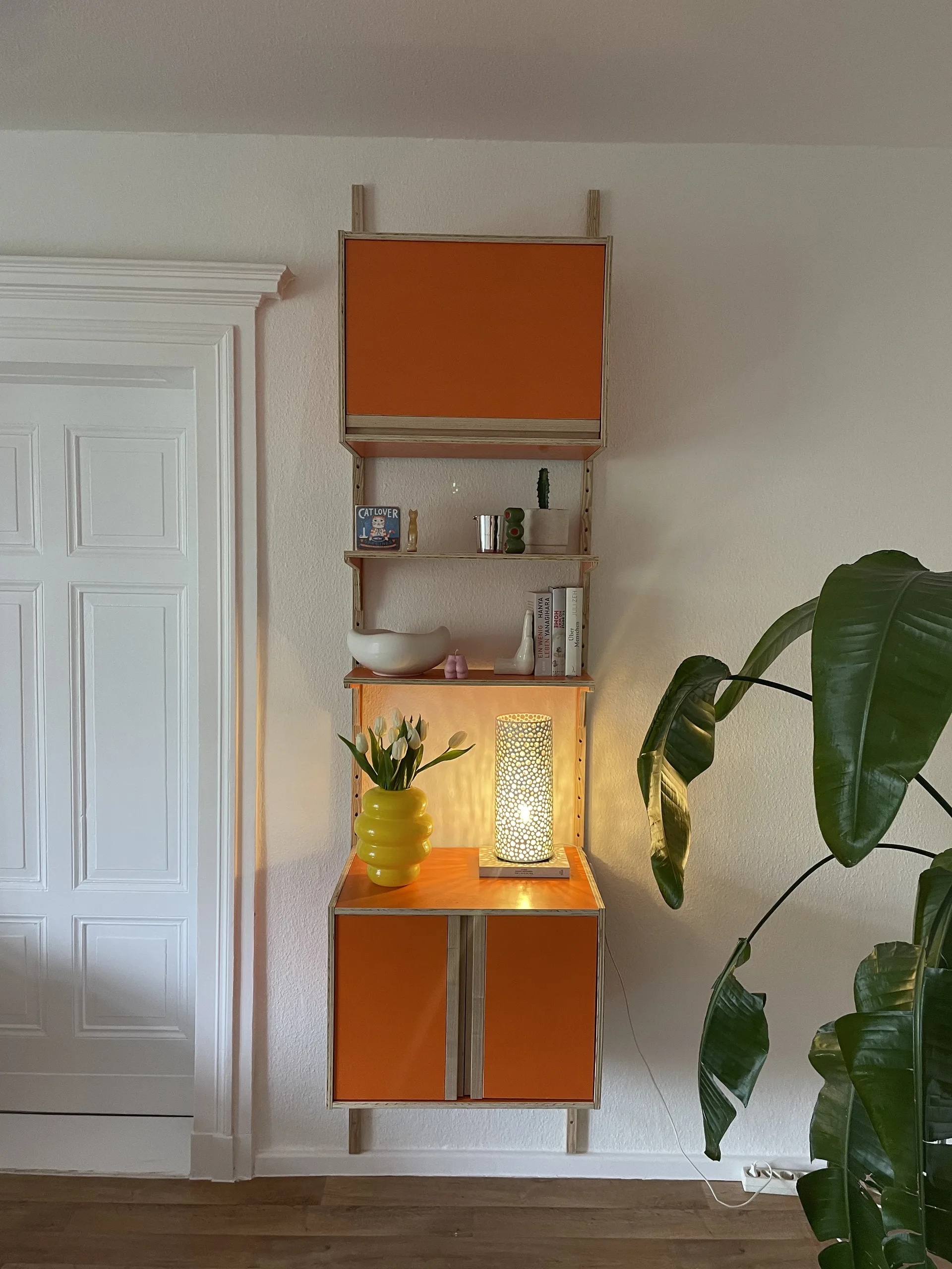 VITIS Orange — vertikale Wandkonfiguration zwischen klassischer Tür und Monstera, Lampe leuchtet warm